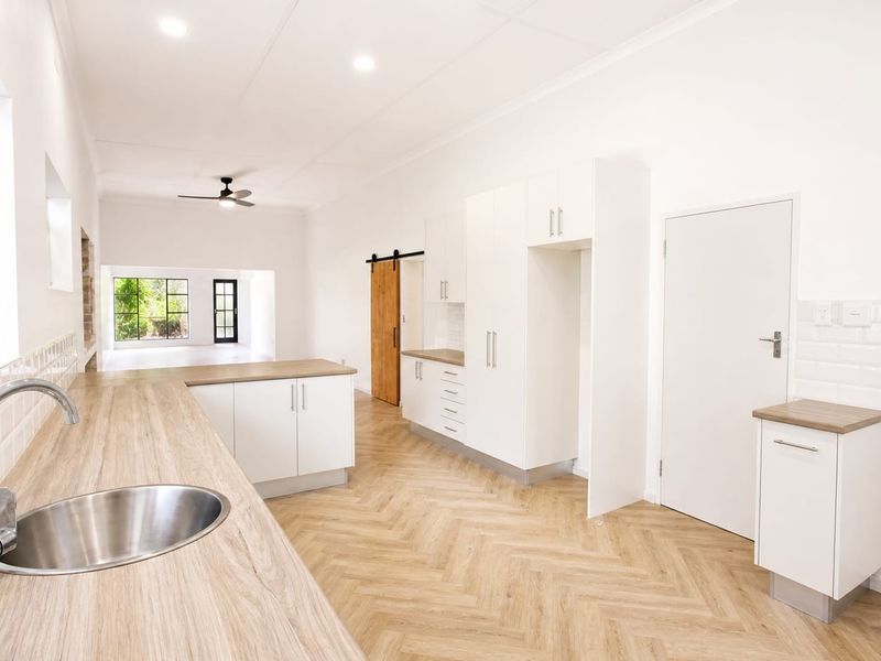 A bright, modern kitchen featuring white cabinetry, subway tile backsplash, wood-look countertops, and herringbone flooring, leading into an open-plan living area.
