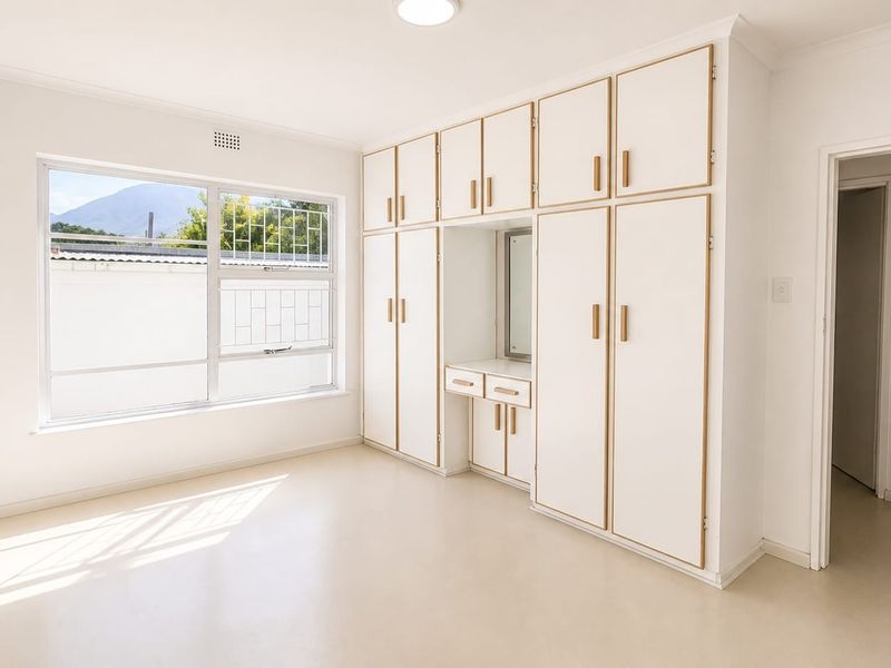 A bright, empty bedroom featuring extensive built-in cabinetry with an integrated vanity unit and large window providing natural light.
