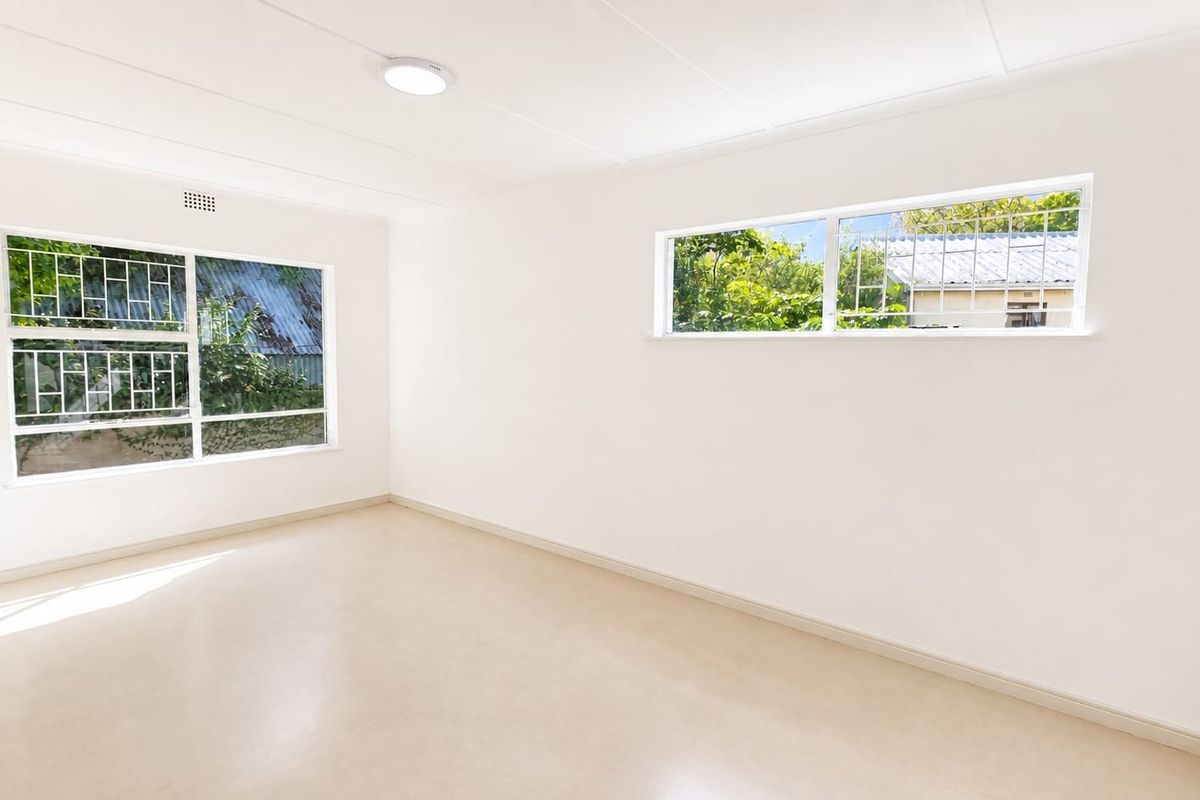 A bright, empty bedroom featuring neutral vinyl flooring, clean white walls, and windows fitted with security bars.