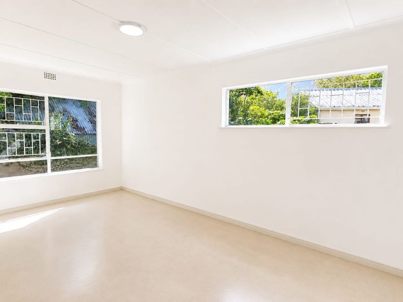 A bright, empty bedroom featuring neutral vinyl flooring, clean white walls, and windows fitted with security bars.