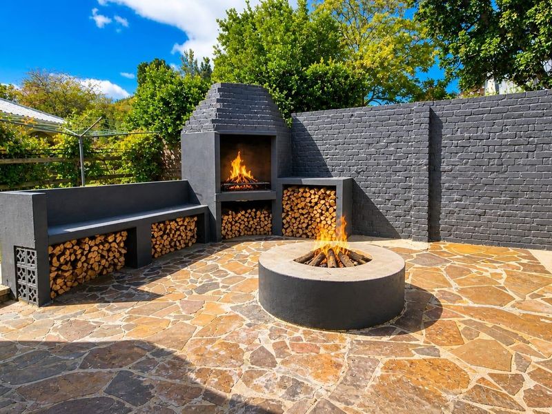 Outdoor entertainment area featuring a stone-paved patio, built-in fireplace, fire pit, and integrated bench seating against a painted brick boundary wall.