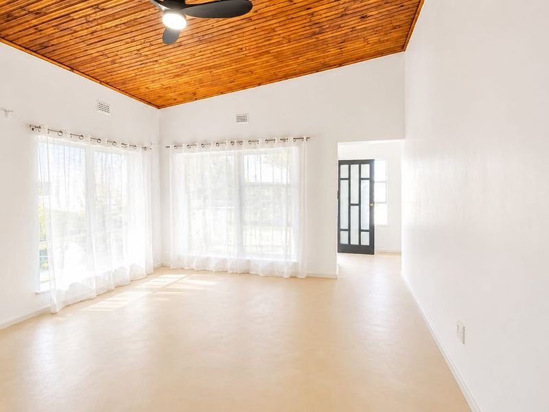 A bright, spacious living area featuring a warm timber-clad ceiling, ceiling fan, and large windows that provide ample natural light.