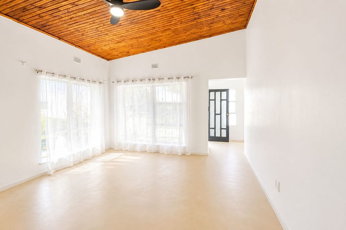 A bright, spacious living area featuring a warm timber-clad ceiling, ceiling fan, and large windows that provide ample natural light.