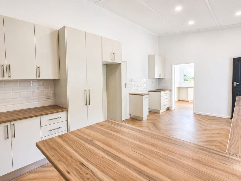 A bright, modern kitchen featuring neutral cabinetry, wood-look laminate countertops, subway tile backsplash, and herringbone flooring, with an open layout leading to an adjacent room.