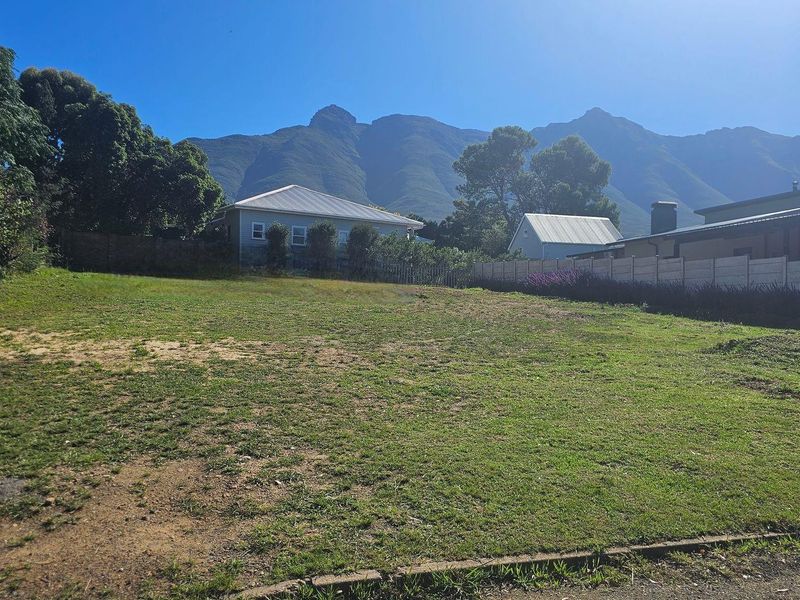 A vacant residential plot featuring a grassed surface, enclosed by a precast concrete boundary wall, offering scenic mountain views.