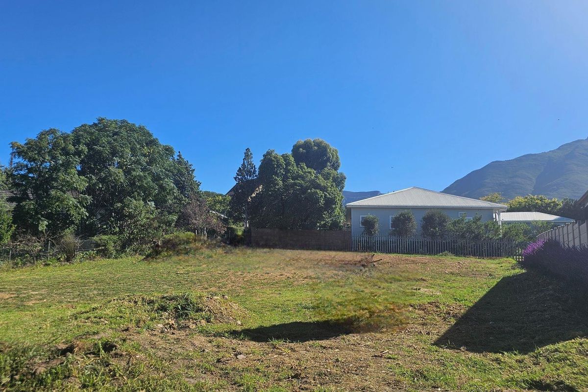 A vacant residential plot featuring established trees, perimeter fencing, and a clear view of the surrounding mountain landscape.