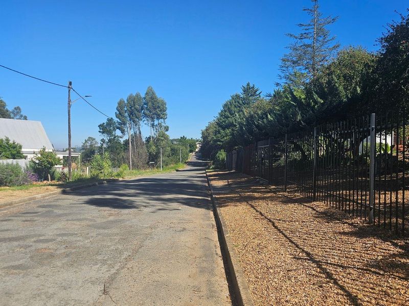A view of the residential street frontage featuring an asphalt road, concrete curbing, and established metal perimeter fencing along the property boundary.