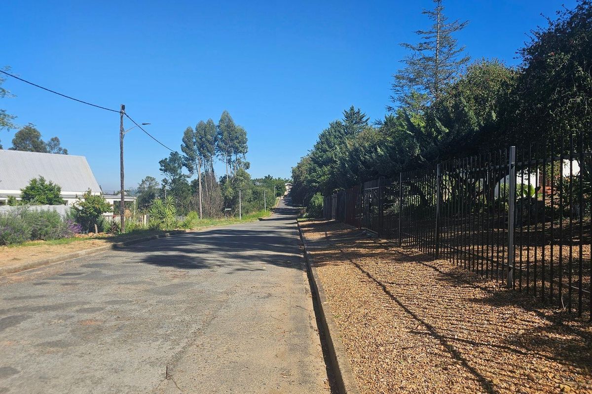 A view of the residential street frontage featuring an asphalt road, concrete curbing, and established metal perimeter fencing along the property boundary.