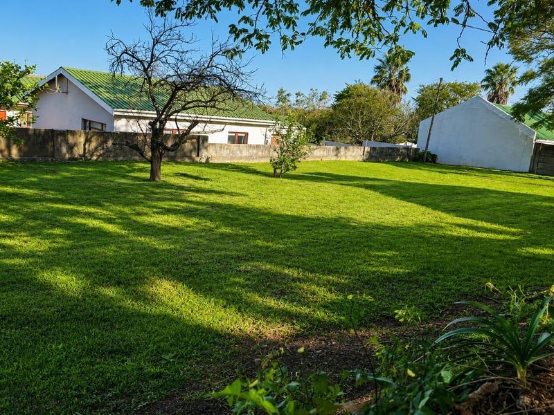 A spacious, well-maintained residential garden featuring an expansive lawn, mature trees, and secure perimeter boundary walls.