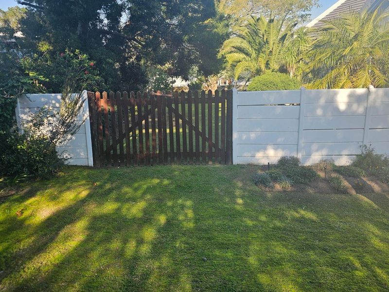 A private garden area featuring a well-maintained lawn, enclosed by a combination of precast concrete walling and a timber picket gate.
