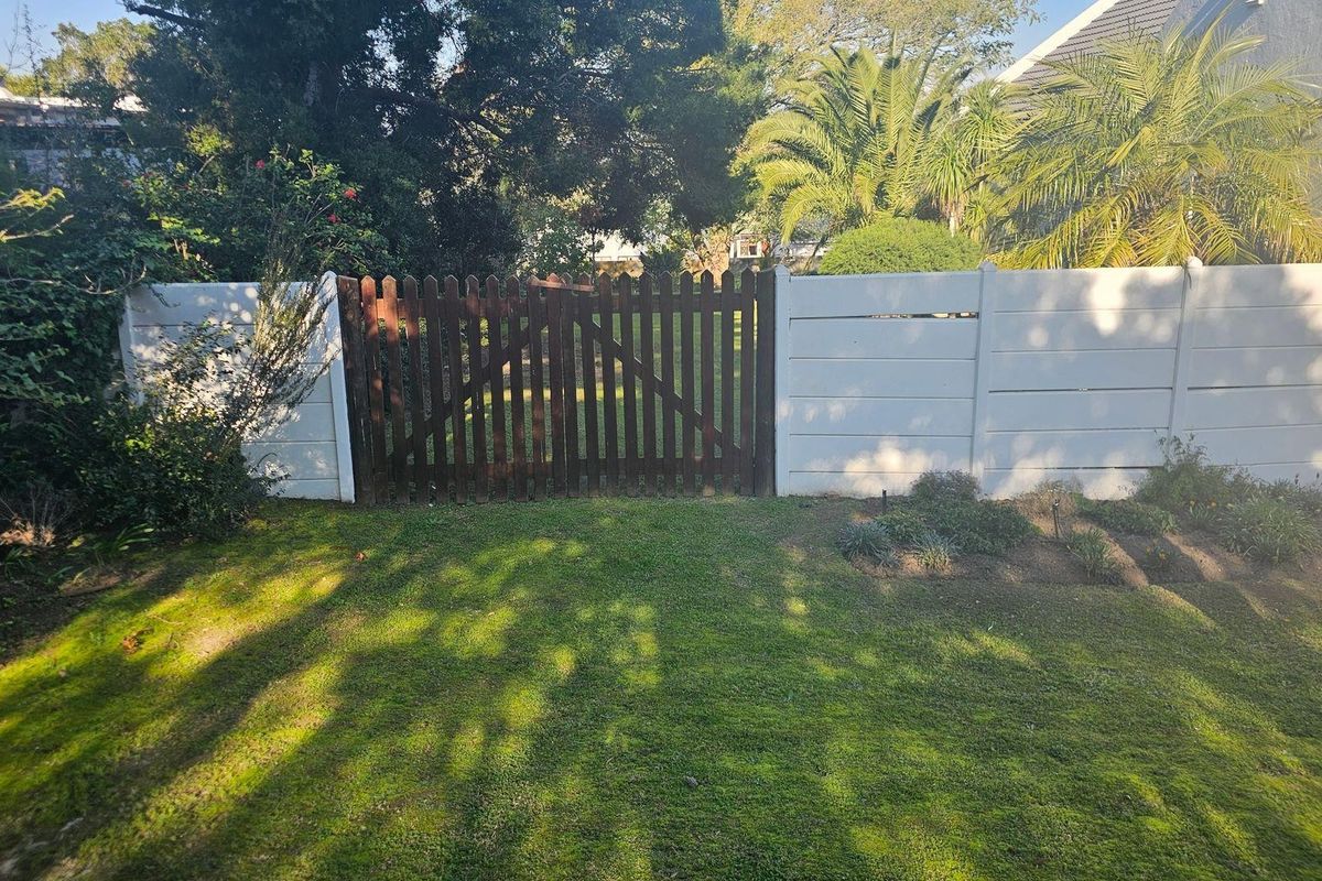 A private garden area featuring a well-maintained lawn, enclosed by a combination of precast concrete walling and a timber picket gate.