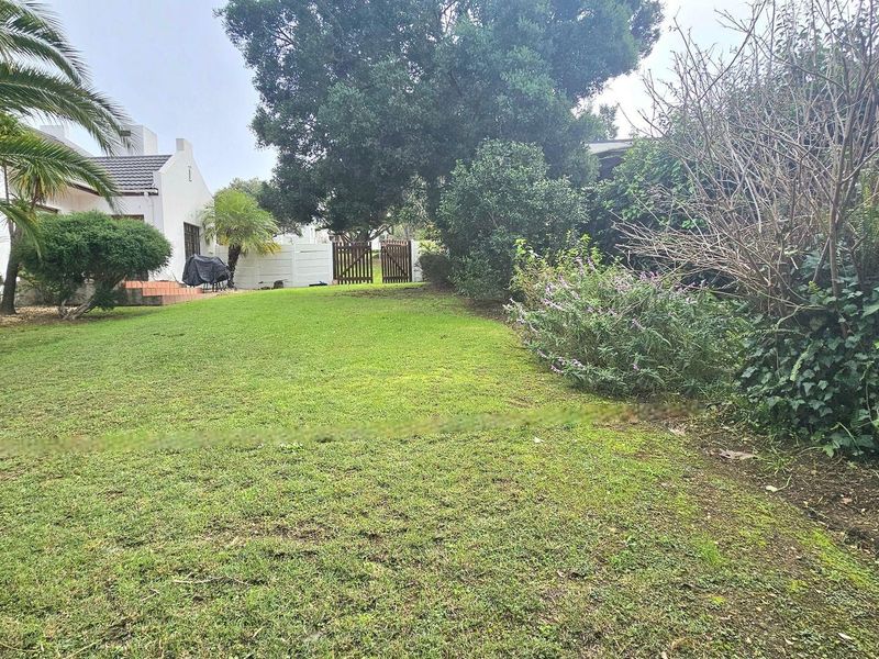 A spacious residential garden featuring a well-maintained lawn, mature trees, and a secure boundary fence with a wooden gate.