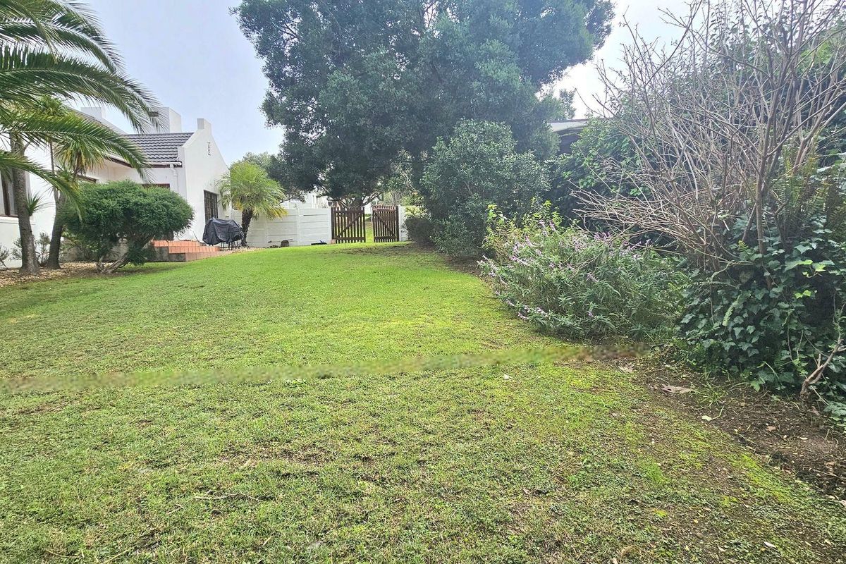A spacious residential garden featuring a well-maintained lawn, mature trees, and a secure boundary fence with a wooden gate.