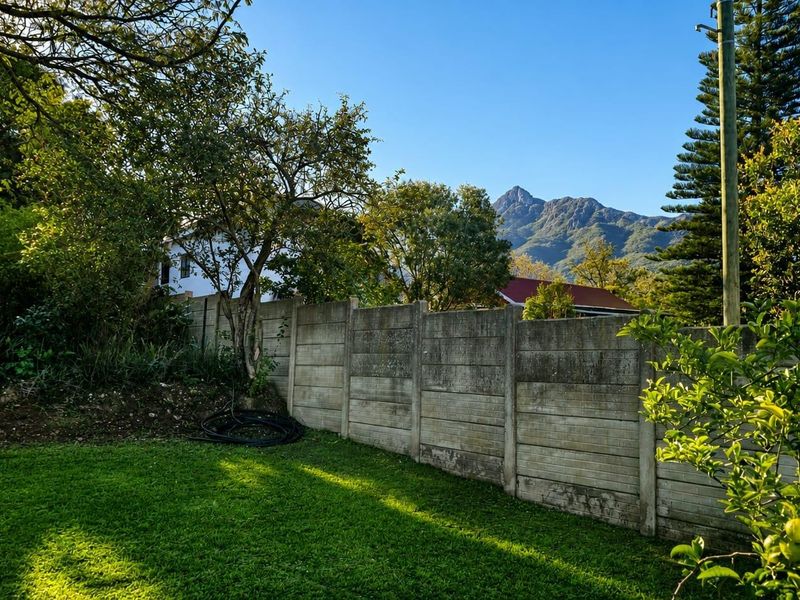 A well-maintained residential garden featuring a precast concrete boundary wall and scenic mountain views in the background.