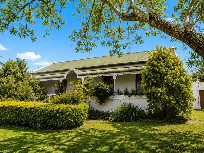 Charming historic-style house featuring a classic corrugated iron roof, a covered veranda with decorative fretwork, and a well-maintained landscaped garden.