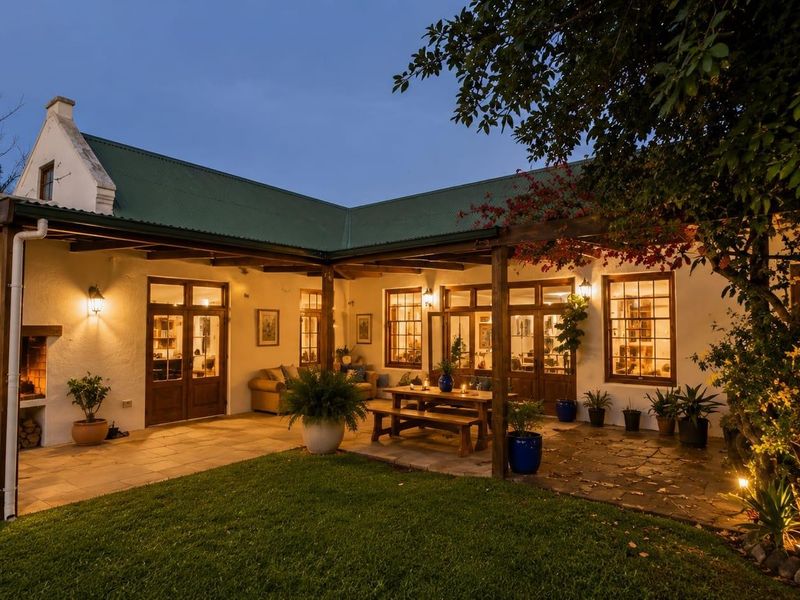 A charming rear patio area featuring a built-in fireplace, timber pergola, and stone paving, seamlessly connecting to the home through timber-framed glass doors.
