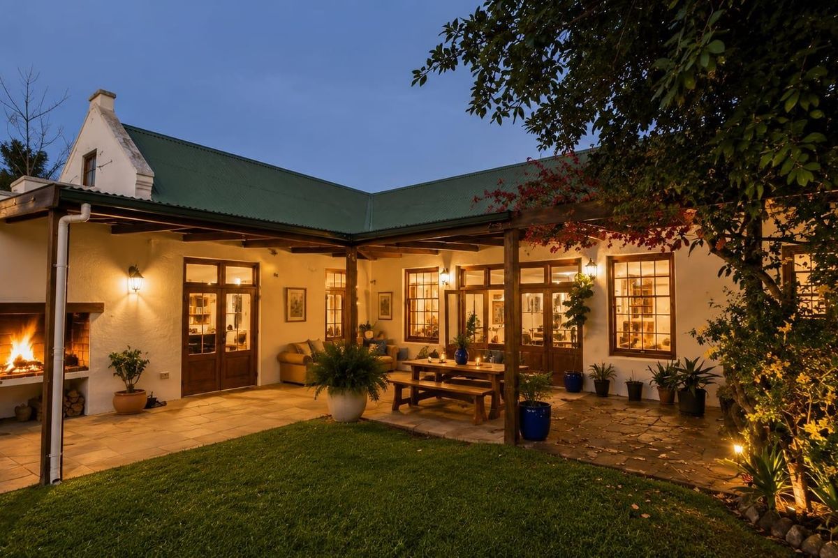 A charming rear patio area featuring a built-in fireplace, timber pergola, and stone paving, seamlessly connecting to the home through timber-framed glass doors.