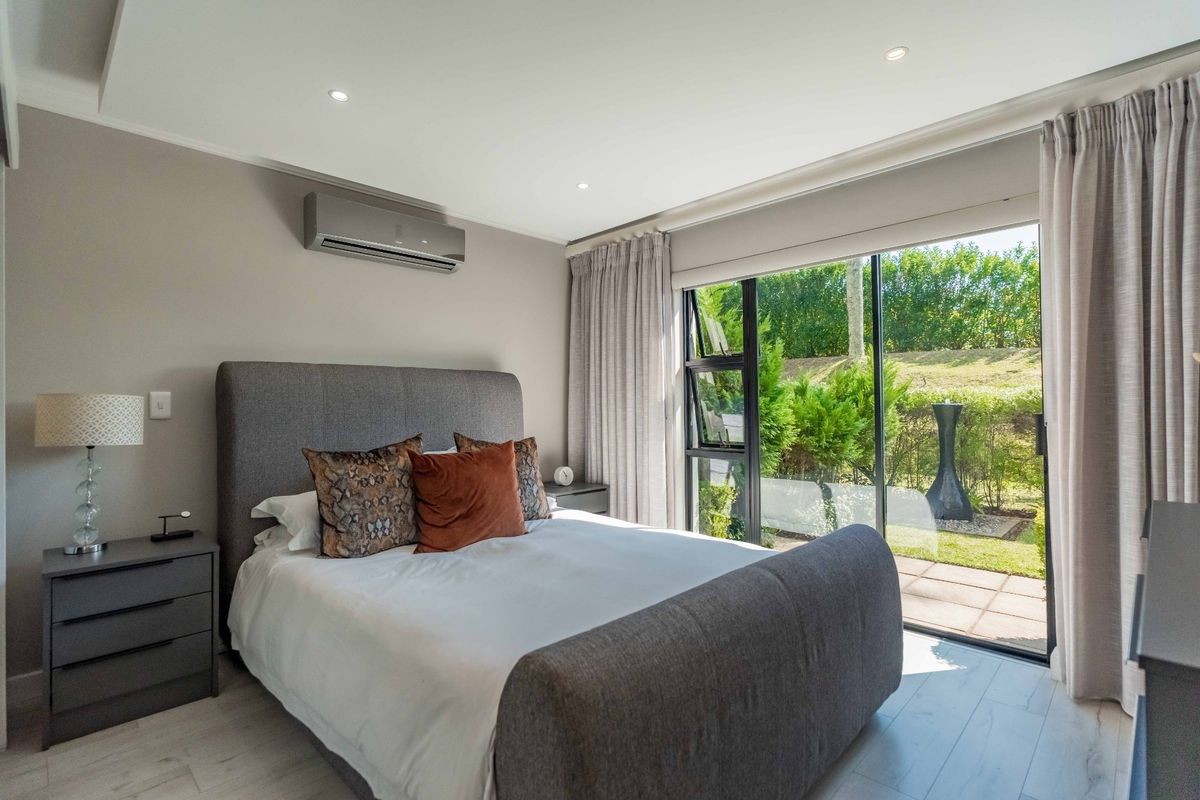 Modern bedroom featuring recessed lighting, a wall-mounted air conditioning unit, and large sliding glass doors providing direct access to the garden area.