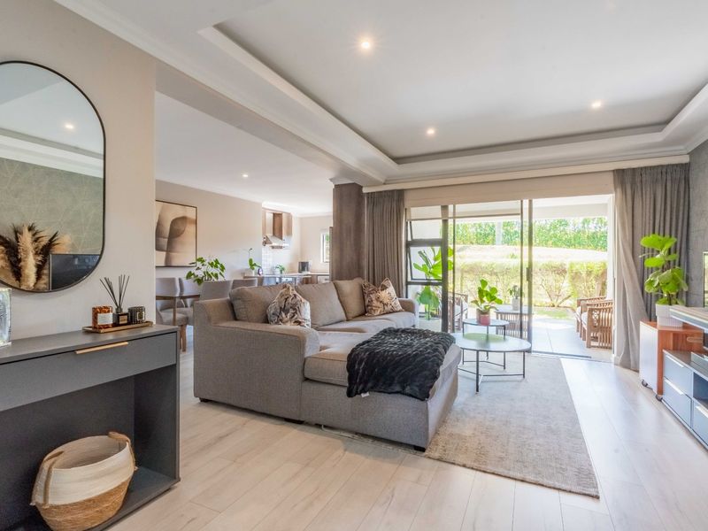 Spacious open-plan living area featuring recessed ceilings, modern downlights, and large sliding glass doors that provide seamless access to the outdoor patio.
