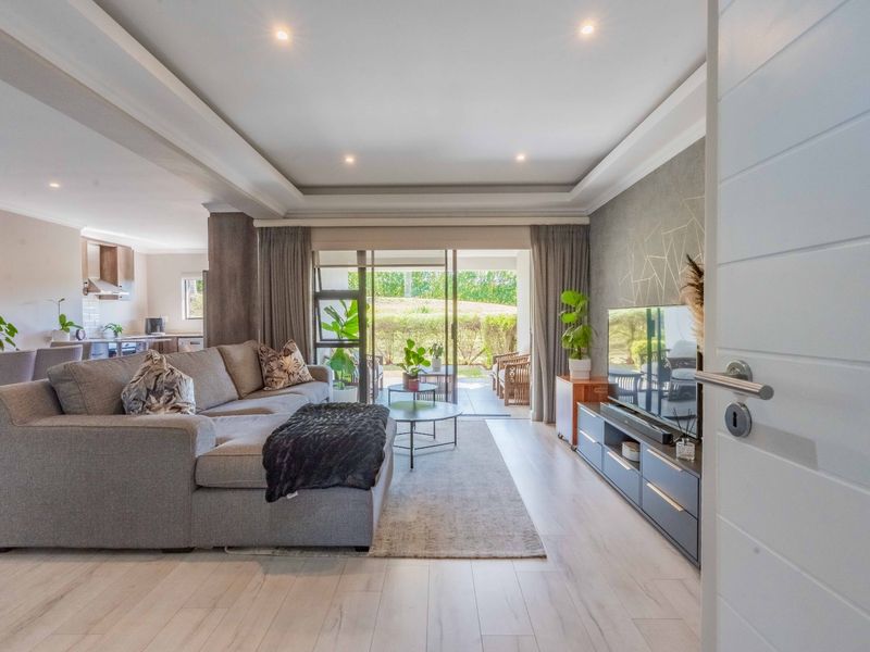 Spacious open-plan living area featuring modern laminate flooring, a tray ceiling with recessed lighting, and seamless flow to an outdoor patio.