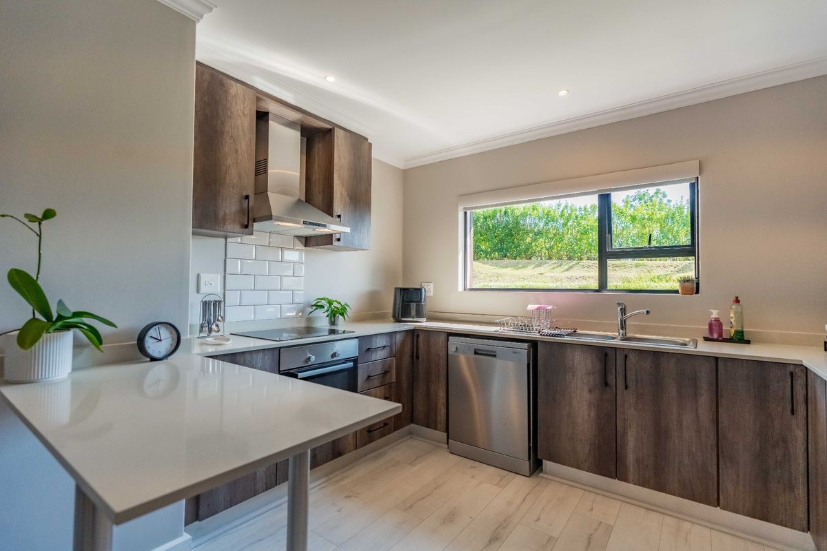 Modern kitchen featuring dark wood cabinetry, stone countertops, subway tile backsplash, integrated appliances, and a breakfast bar area with natural light.