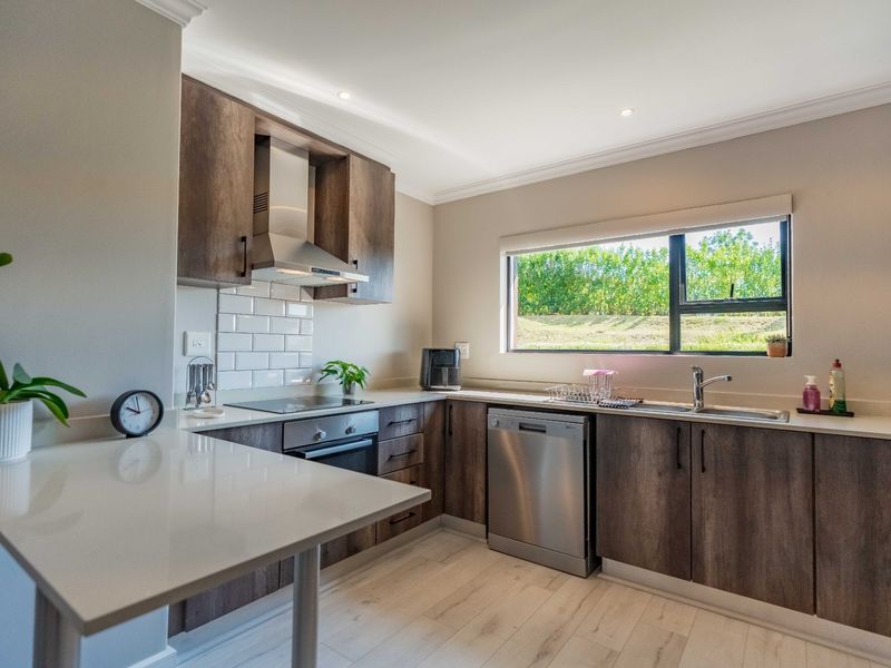 Modern kitchen featuring dark wood cabinetry, stone countertops, subway tile backsplash, integrated appliances, and a breakfast bar area with natural light.