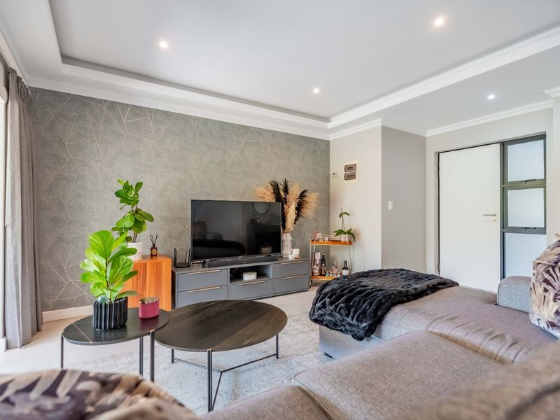 A modern, well-maintained living room featuring a recessed ceiling with downlights, a stylish feature wall, and large sliding glass doors providing natural light.