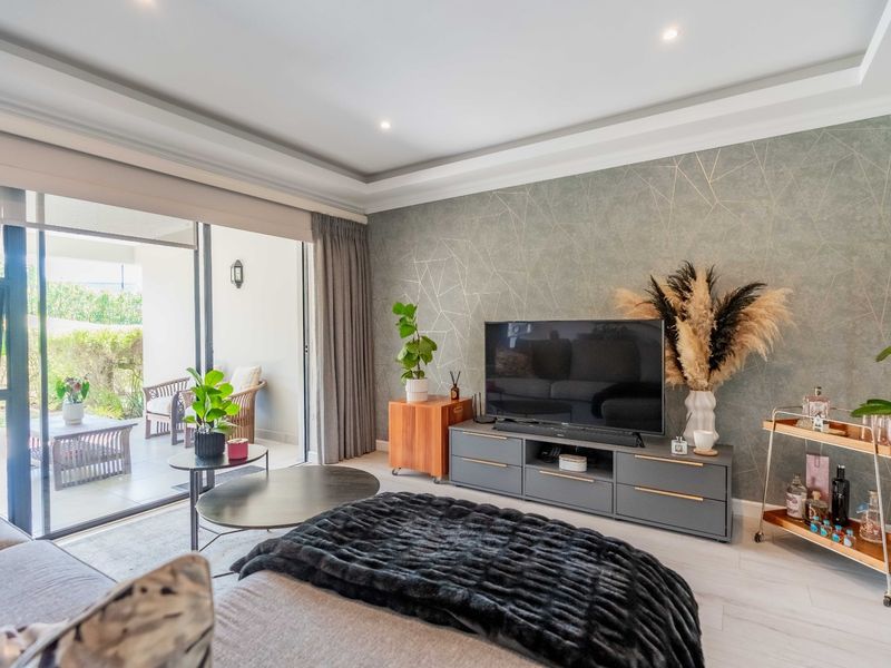 Modern living room featuring a decorative feature wall, recessed ceiling lighting, and large sliding glass doors providing seamless access to the outdoor patio area.