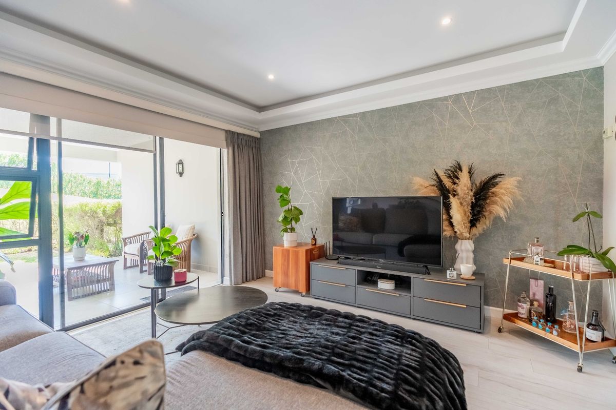 Modern living room featuring a decorative feature wall, recessed ceiling lighting, and large sliding glass doors providing seamless access to the outdoor patio area.