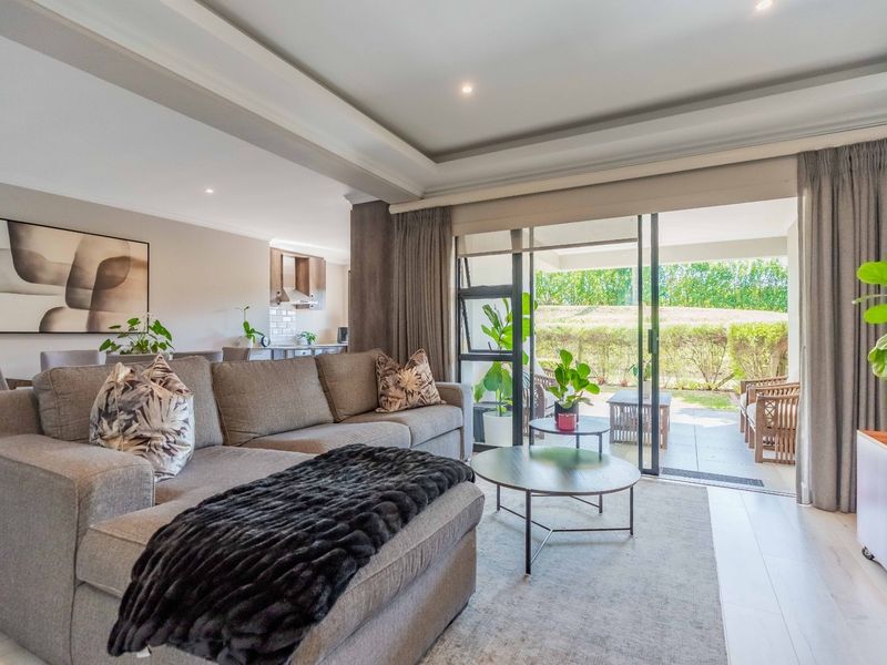 Spacious open-plan living area featuring a modern kitchen, recessed ceiling lighting, and seamless flow to a private tiled patio through large sliding glass doors.