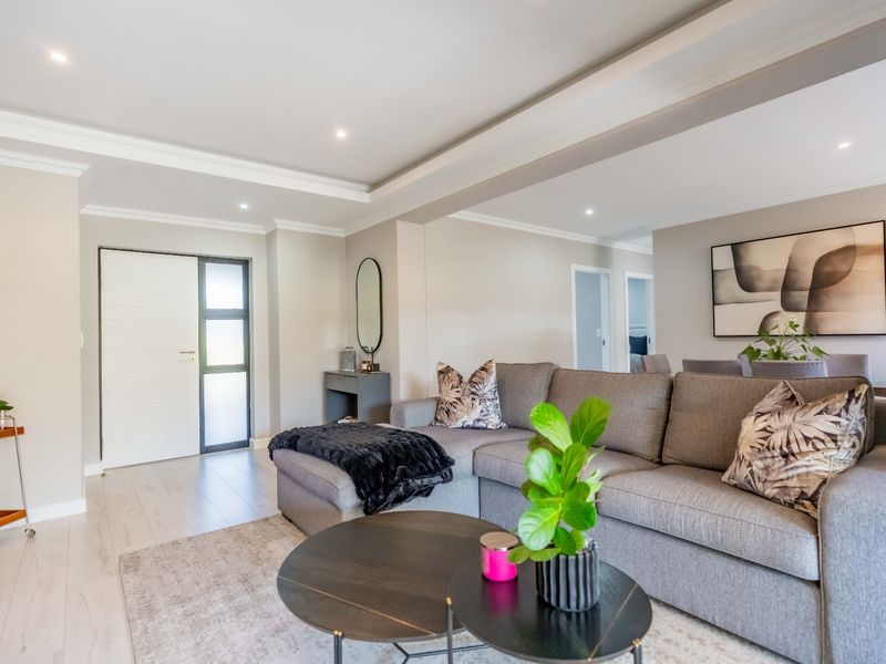 A bright and modern open-plan living area featuring neutral tones, recessed ceiling lighting, cove molding, and high-quality laminate flooring.