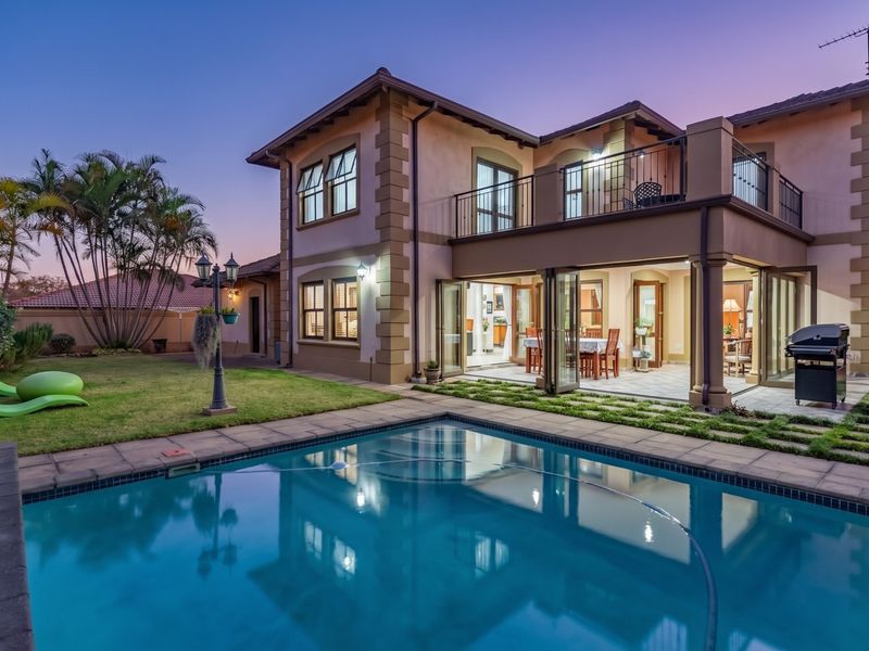 Rear view of a two-story house featuring a swimming pool, landscaped garden, covered patio with sliding doors, and an upper-level balcony.