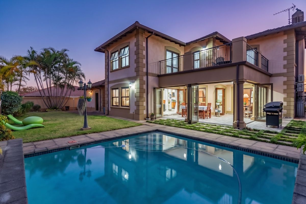 Rear view of a two-story house featuring a swimming pool, landscaped garden, covered patio with sliding doors, and an upper-level balcony.