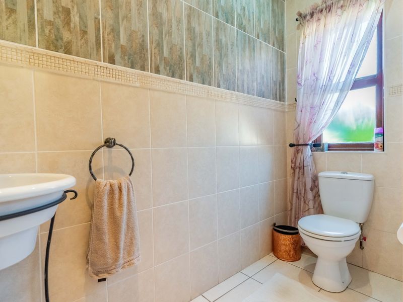 A functional bathroom featuring tiled walls, a wall-mounted basin, and a standard toilet, with natural light provided by a window.