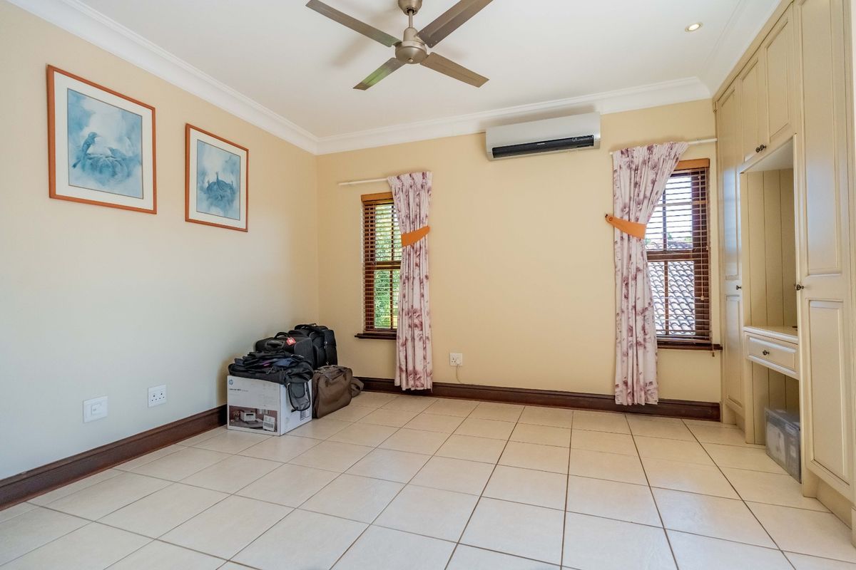 A spacious bedroom featuring tiled flooring, built-in cupboards, a ceiling fan, and a split-system air conditioner.
