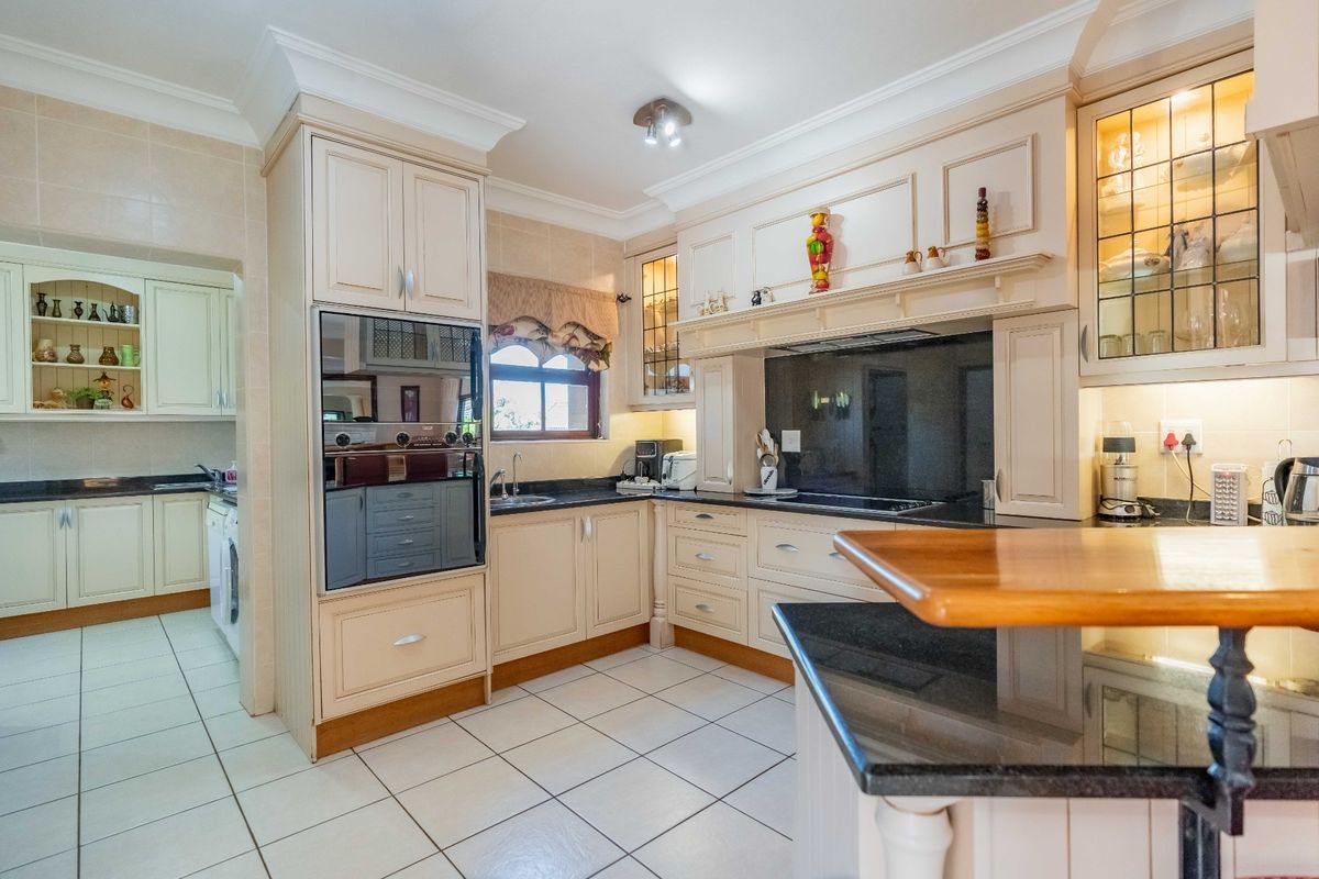 A well-appointed kitchen featuring cream cabinetry, dark granite countertops, integrated appliances, and tiled flooring, with an adjacent scullery area.
