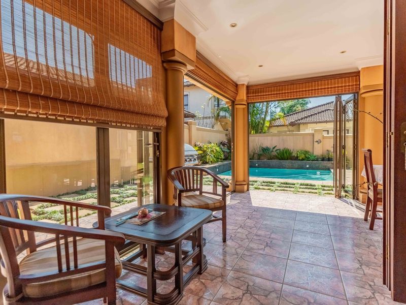 Covered patio area featuring tiled flooring and folding glass doors, providing seamless access to the outdoor swimming pool and garden space.