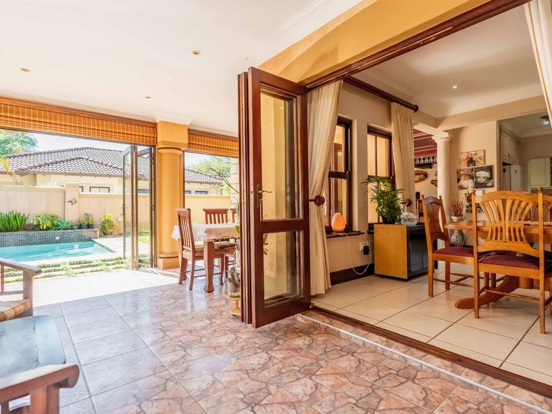 A covered patio area featuring tiled flooring and folding glass doors that open directly onto a swimming pool and garden space.