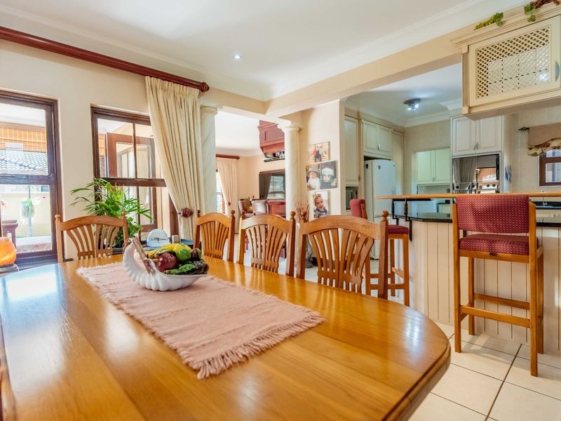 Open plan dining area flowing into a functional kitchen with breakfast bar, tiled floors, and classic cabinetry.