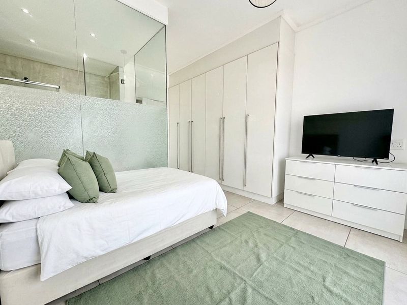 Modern bedroom featuring built-in cupboards, tiled flooring, and a contemporary glass partition wall separating the sleeping area from the en-suite bathroom.