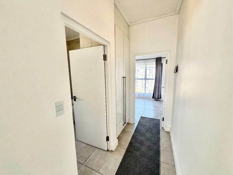 A clean, well-maintained hallway featuring neutral tiled flooring and built-in storage cupboards, providing access to adjacent rooms.