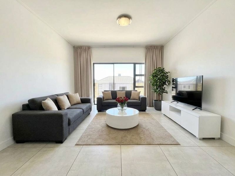 A bright and well-maintained living room featuring neutral tiled flooring, clean white walls, and a large sliding glass door providing natural light.