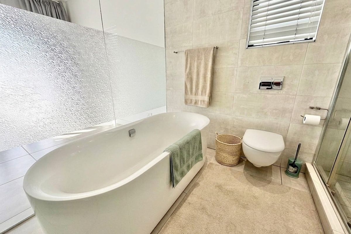 Modern bathroom featuring a sleek freestanding bathtub, wall-mounted toilet, glass shower enclosure, and neutral wall tiling with contemporary fixtures.