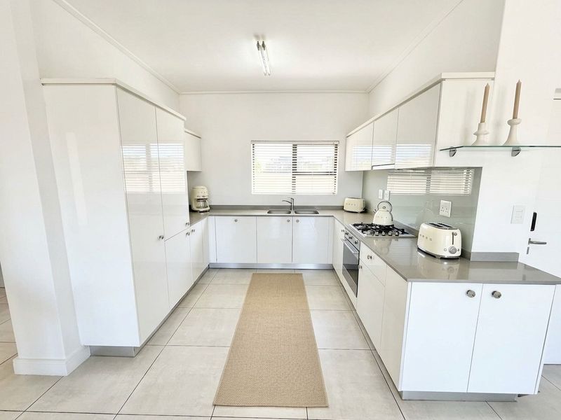 Modern U-shaped kitchen featuring high-gloss white cabinetry, stone countertops, integrated gas hob, built-in oven, and neutral tiled flooring.