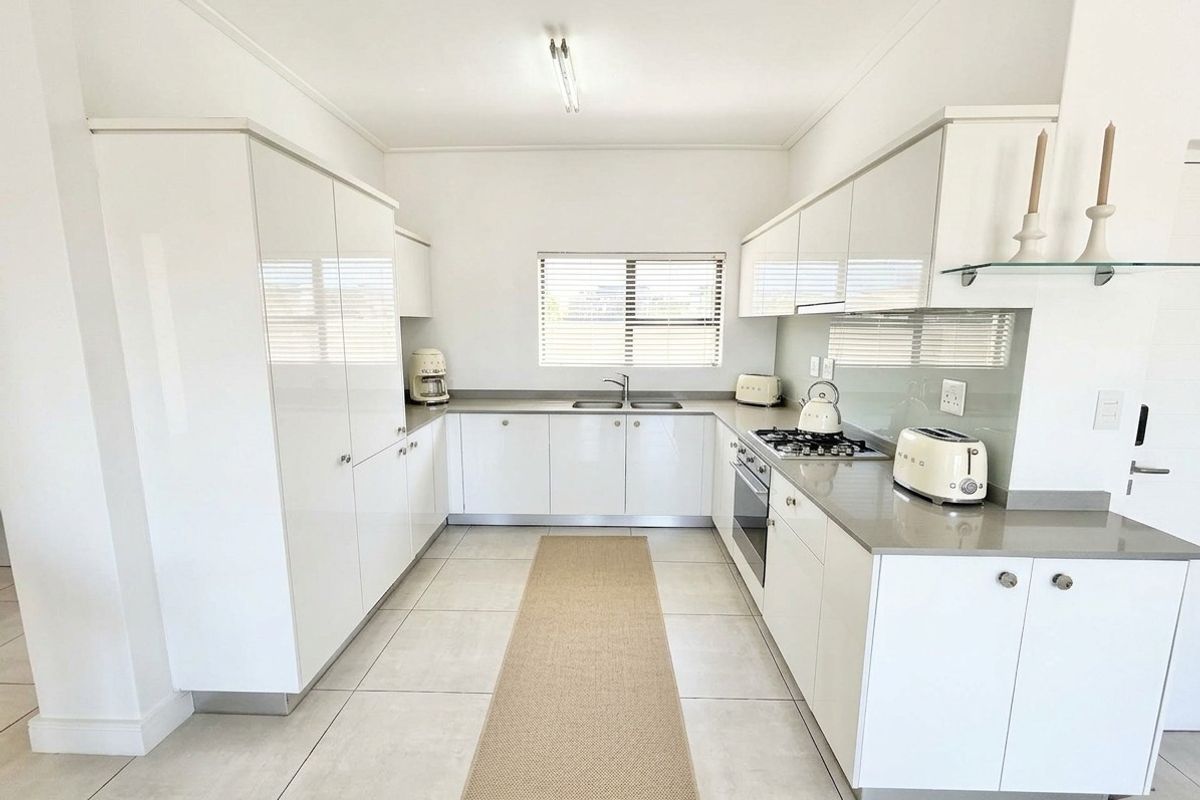 Modern U-shaped kitchen featuring high-gloss white cabinetry, stone countertops, integrated gas hob, built-in oven, and neutral tiled flooring.