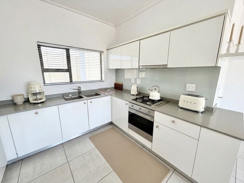 Modern kitchen featuring white high-gloss cabinetry, stone countertops, integrated gas hob, built-in oven, and sleek glass splashback with neutral floor tiles.