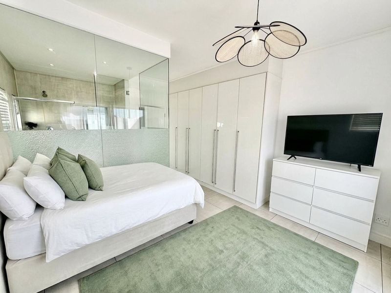 Modern bedroom featuring built-in cupboards, tiled flooring, and a contemporary glass partition wall separating the en-suite bathroom area.