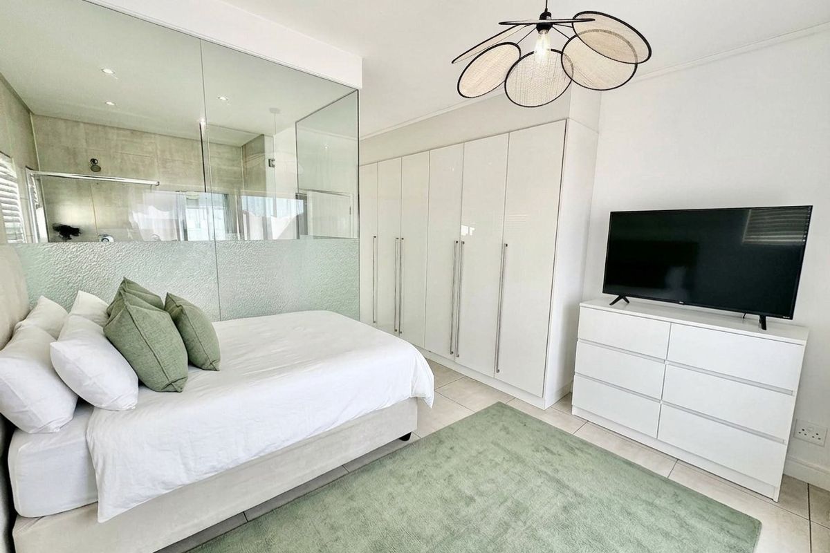 Modern bedroom featuring built-in cupboards, tiled flooring, and a contemporary glass partition wall separating the en-suite bathroom area.