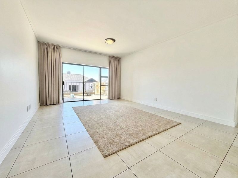 A bright, open-plan living area featuring neutral tiled flooring and a large sliding glass door providing access to an outdoor space.