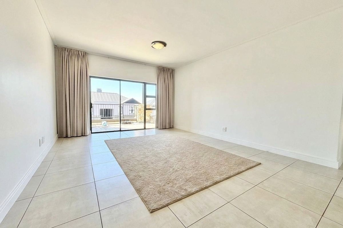 A bright, open-plan living area featuring neutral tiled flooring and a large sliding glass door providing access to an outdoor space.